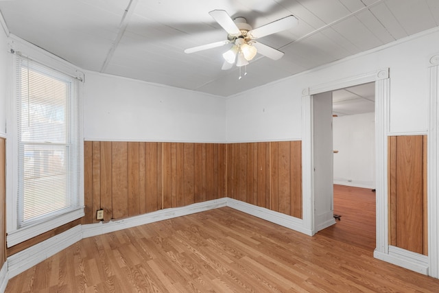 empty room with hardwood / wood-style floors, ceiling fan, ornamental molding, and wood walls