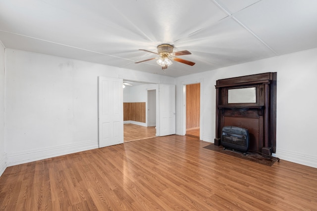 unfurnished living room featuring wood-type flooring, a wood stove, and ceiling fan