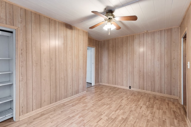 spare room featuring ceiling fan, wood walls, and light wood-type flooring