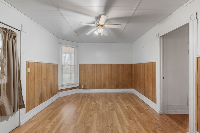 empty room with light hardwood / wood-style flooring, ceiling fan, crown molding, and wood walls