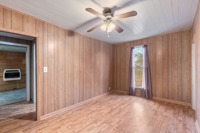 spare room featuring ceiling fan, light hardwood / wood-style floors, heating unit, and wood walls