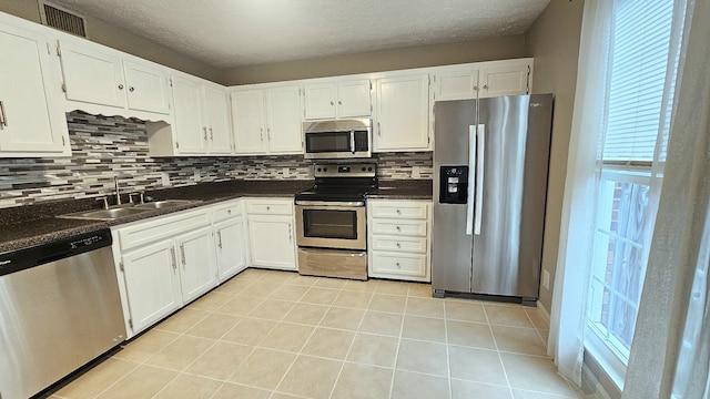 kitchen with appliances with stainless steel finishes, tasteful backsplash, dark stone counters, sink, and white cabinets