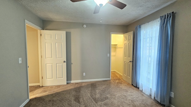 unfurnished bedroom with carpet, a textured ceiling, ceiling fan, a spacious closet, and a closet