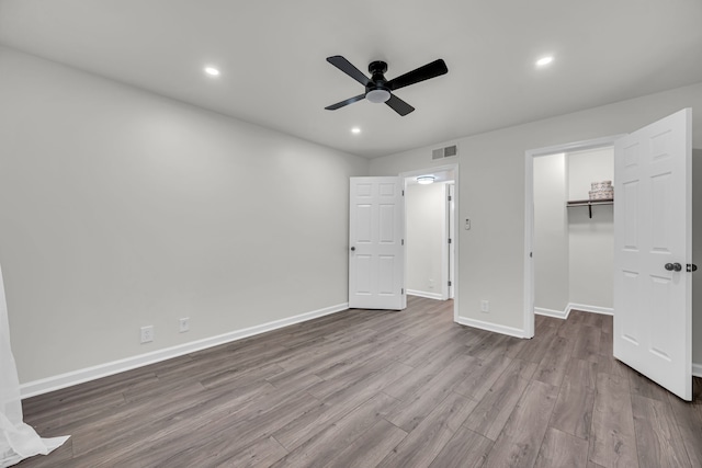 unfurnished bedroom with a walk in closet, ceiling fan, a closet, and light wood-type flooring