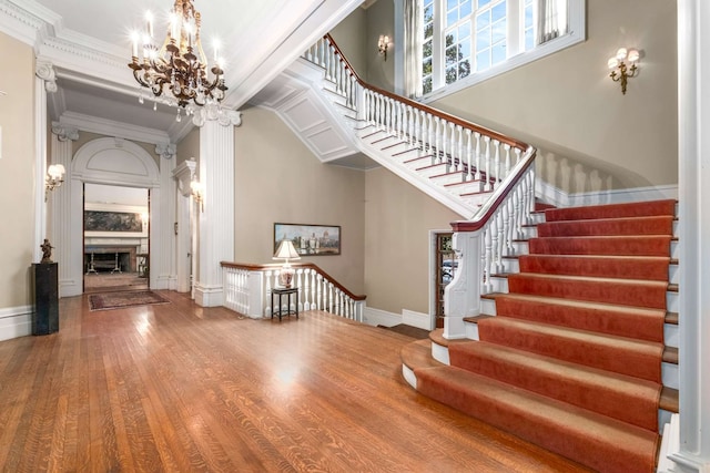 staircase with a notable chandelier, wood-type flooring, and ornamental molding