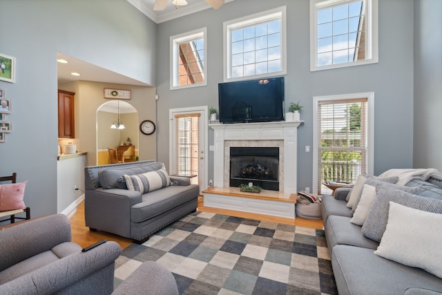 living room with light wood-type flooring, a towering ceiling, ornamental molding, ceiling fan, and a fireplace