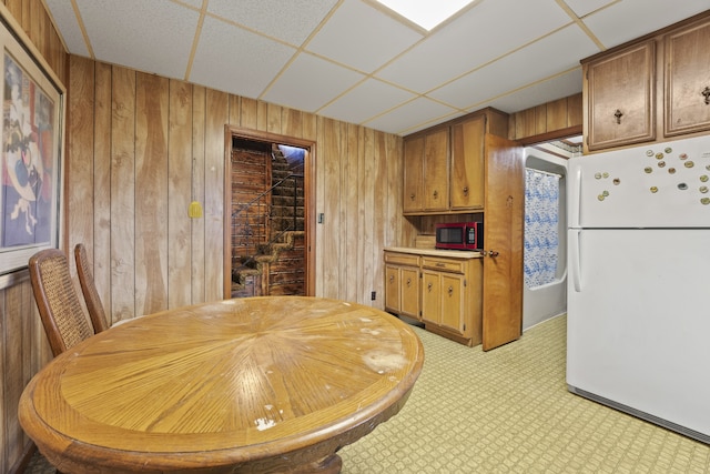 kitchen with white fridge, a drop ceiling, and wood walls