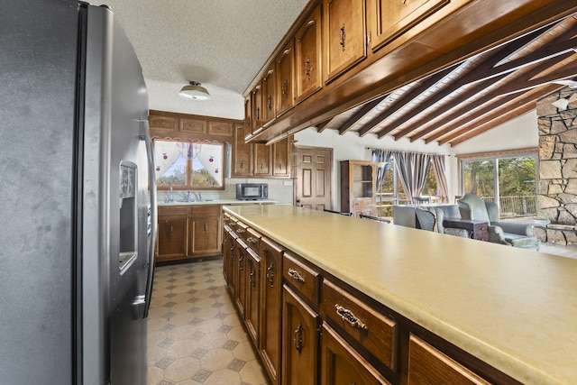 kitchen featuring a textured ceiling, vaulted ceiling with beams, stainless steel fridge, and sink