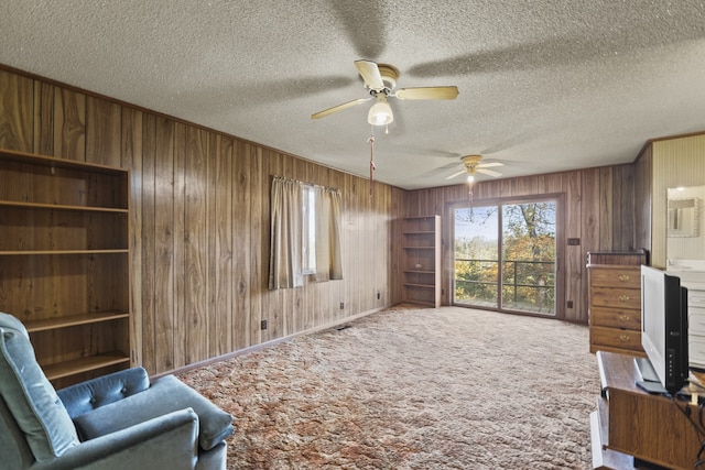 living area featuring ceiling fan, wood walls, carpet floors, and a textured ceiling