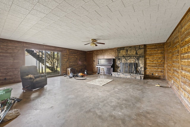 unfurnished living room featuring ceiling fan, a fireplace, concrete floors, and wood walls