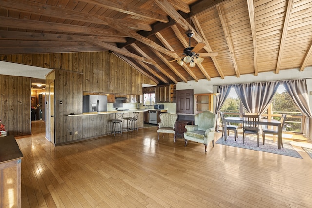 unfurnished living room featuring beam ceiling, ceiling fan, wooden ceiling, light hardwood / wood-style floors, and wooden walls