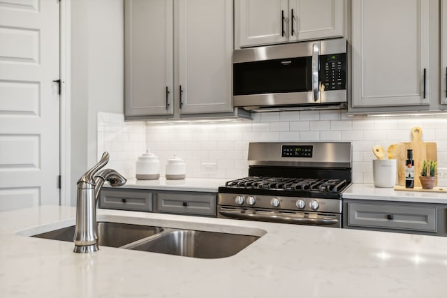 kitchen with sink, gray cabinetry, stainless steel appliances, light stone countertops, and decorative backsplash