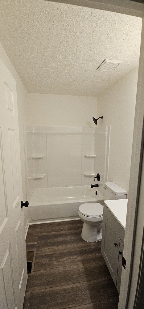 full bathroom featuring washtub / shower combination, hardwood / wood-style floors, a textured ceiling, toilet, and vanity