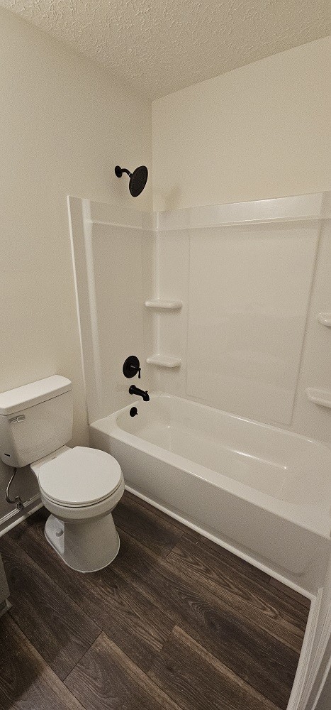 bathroom featuring hardwood / wood-style floors, a textured ceiling, shower / bath combination, and toilet