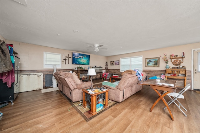 living room with a textured ceiling, light wood-type flooring, ceiling fan, and wood walls