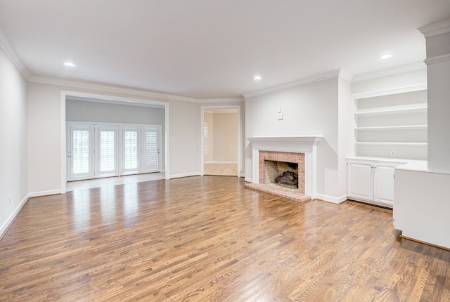 unfurnished living room featuring hardwood / wood-style flooring, built in features, crown molding, and a brick fireplace