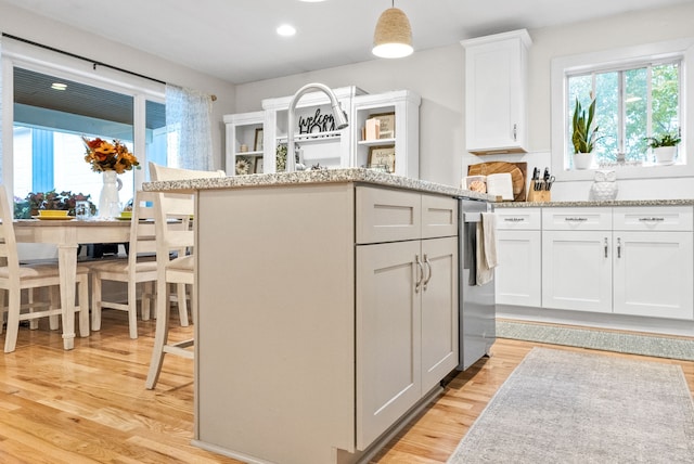 kitchen with stainless steel dishwasher, light wood-type flooring, decorative light fixtures, a kitchen bar, and white cabinetry