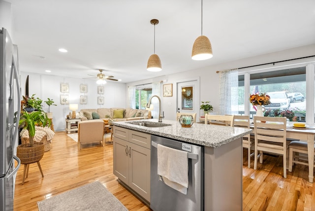 kitchen with pendant lighting, light wood-type flooring, stainless steel appliances, and a kitchen island with sink