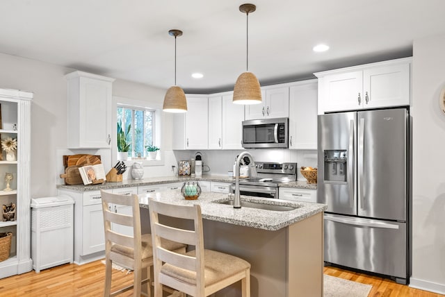 kitchen with white cabinetry, stainless steel appliances, light stone counters, and decorative light fixtures