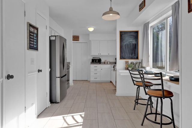 kitchen featuring stainless steel fridge, white cabinetry, and hanging light fixtures