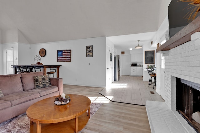 living room featuring lofted ceiling, light wood-type flooring, and a brick fireplace