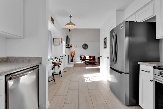 kitchen featuring decorative light fixtures, light wood-type flooring, white cabinetry, and appliances with stainless steel finishes