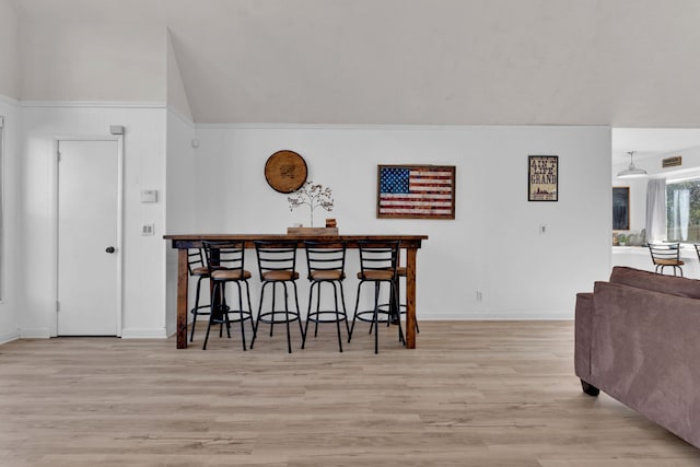 dining area with bar area, vaulted ceiling, crown molding, and light hardwood / wood-style flooring