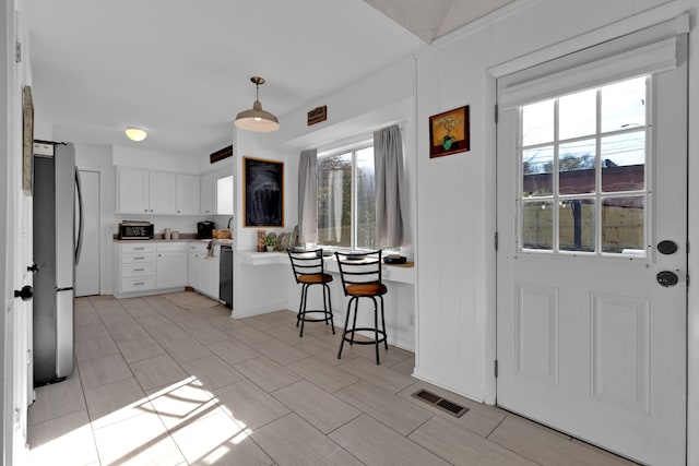 kitchen with a kitchen breakfast bar, pendant lighting, black dishwasher, white cabinetry, and stainless steel refrigerator