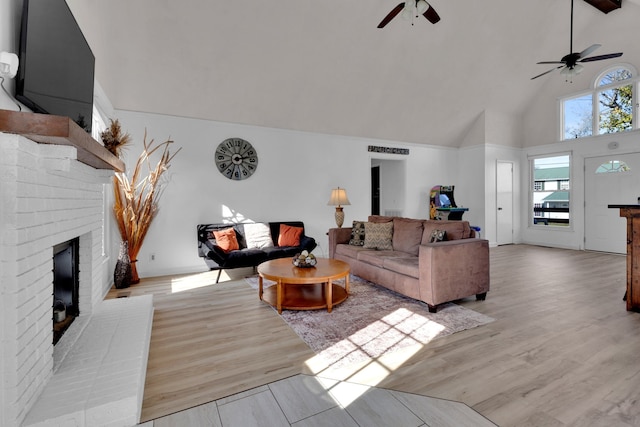 living room featuring a fireplace, light hardwood / wood-style floors, high vaulted ceiling, and ceiling fan