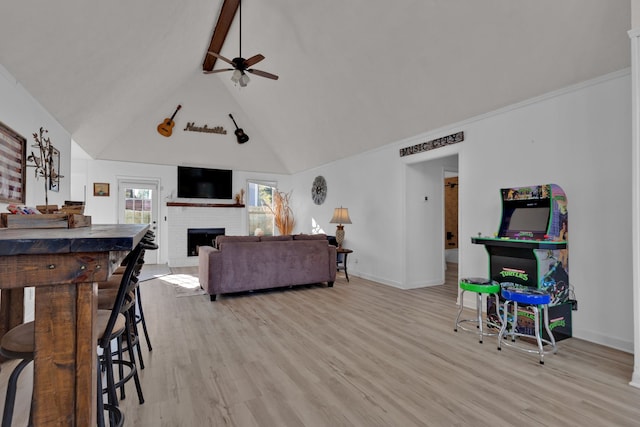 living room with high vaulted ceiling, a brick fireplace, ceiling fan, beam ceiling, and light hardwood / wood-style floors