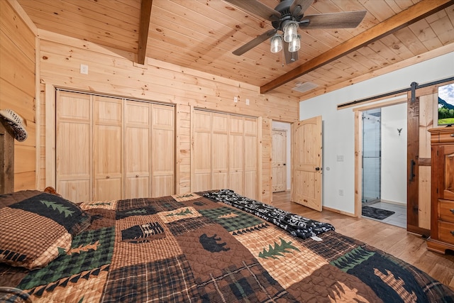 bedroom featuring beamed ceiling, a barn door, and wood walls