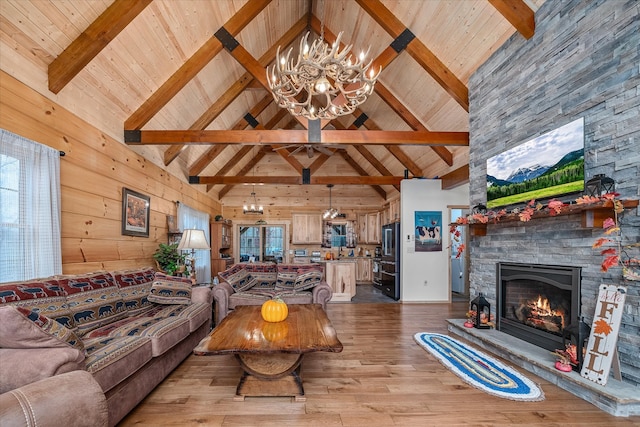 living room with high vaulted ceiling, a stone fireplace, wooden walls, light hardwood / wood-style flooring, and beamed ceiling