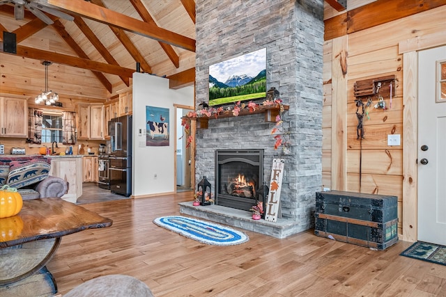 living room featuring beamed ceiling, a stone fireplace, light wood-type flooring, and high vaulted ceiling