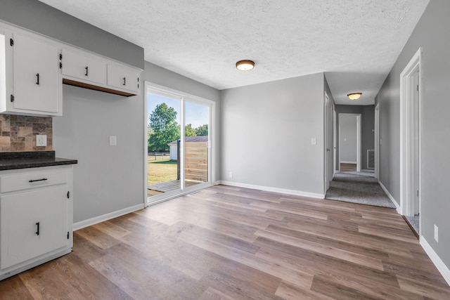 interior space with white cabinets, light hardwood / wood-style floors, and a textured ceiling