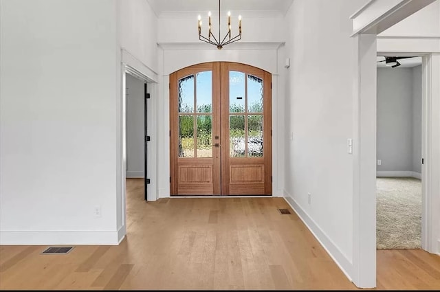 entryway with crown molding, french doors, an inviting chandelier, and light hardwood / wood-style flooring