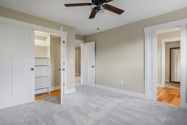 unfurnished bedroom featuring light carpet, a walk in closet, a closet, and ceiling fan