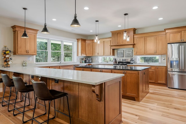 kitchen featuring appliances with stainless steel finishes, light wood-type flooring, a breakfast bar, sink, and hanging light fixtures