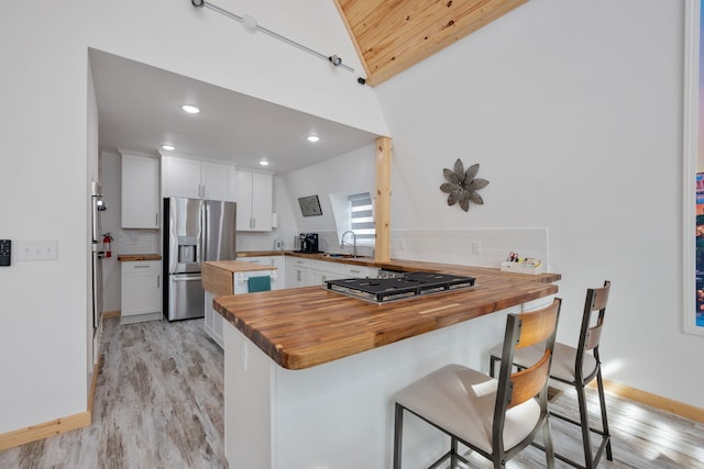 kitchen featuring lofted ceiling, white cabinets, kitchen peninsula, appliances with stainless steel finishes, and butcher block counters