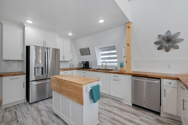 kitchen with stainless steel appliances, white cabinets, wooden counters, and light wood-type flooring