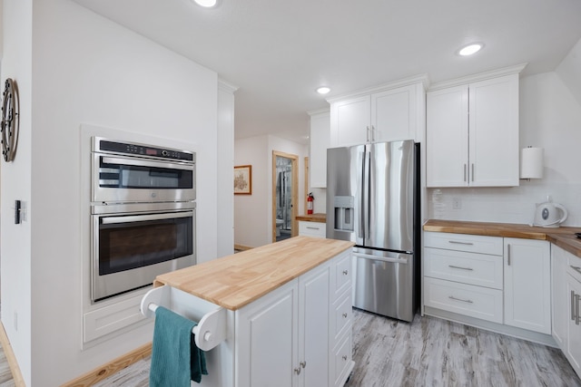 kitchen with white cabinets, wood counters, stainless steel appliances, and light hardwood / wood-style flooring