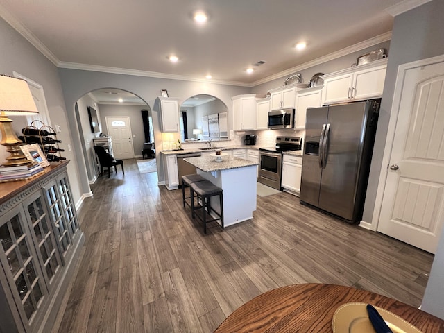 kitchen with a breakfast bar, white cabinetry, stainless steel appliances, a center island, and light stone counters