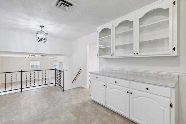 interior space featuring a textured ceiling, white cabinets, decorative light fixtures, and a notable chandelier