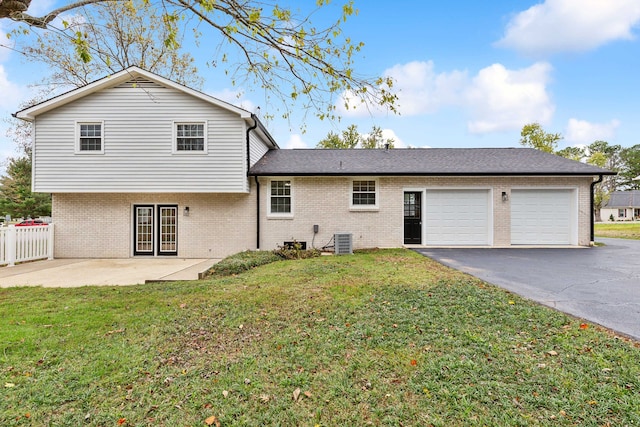 rear view of house featuring a lawn, a garage, and central AC