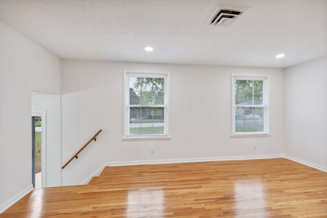 unfurnished room with a healthy amount of sunlight, light hardwood / wood-style floors, and a textured ceiling