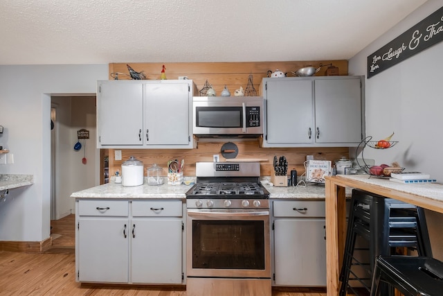 kitchen with light stone countertops, light hardwood / wood-style floors, a textured ceiling, and appliances with stainless steel finishes