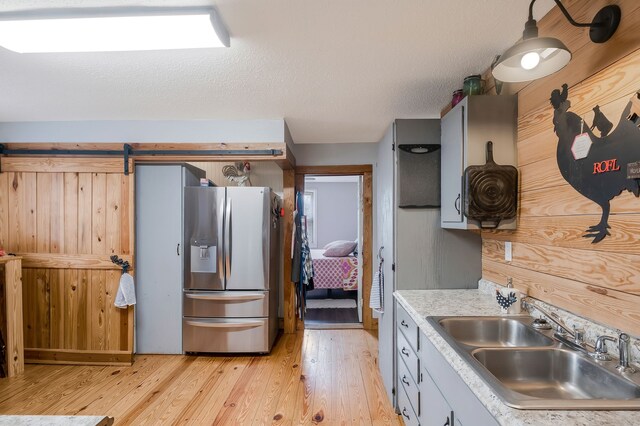 kitchen featuring stainless steel fridge, a textured ceiling, light hardwood / wood-style flooring, and sink