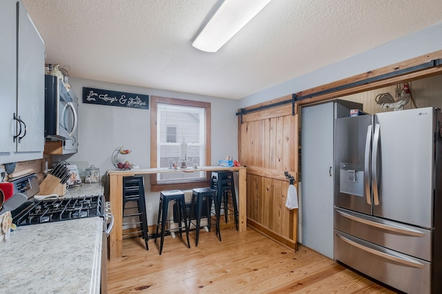 kitchen featuring a barn door, light wood-type flooring, a textured ceiling, and appliances with stainless steel finishes