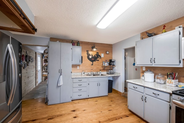 kitchen with light wood-type flooring, a textured ceiling, white appliances, wooden walls, and sink