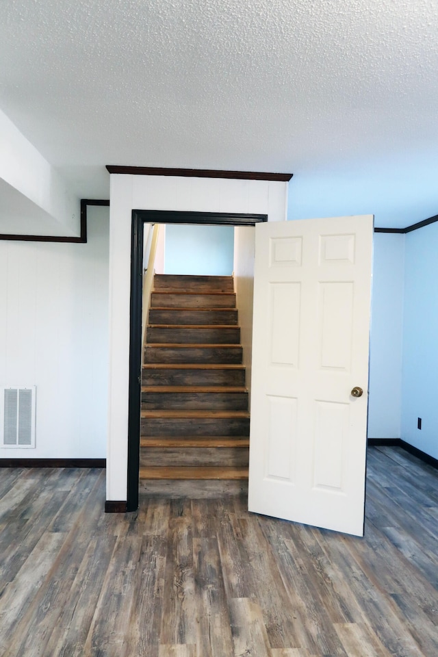 stairway with hardwood / wood-style floors, crown molding, and a textured ceiling