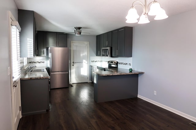 kitchen featuring dark wood-type flooring, hanging light fixtures, tasteful backsplash, ceiling fan with notable chandelier, and appliances with stainless steel finishes